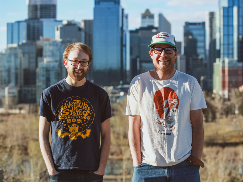 From We Make Radio, longtime volunteers, Cailean David and Greg Chernoff show off their favourite Funding Drive t-shirts from years past | Photo: Courtesy of CJSW
