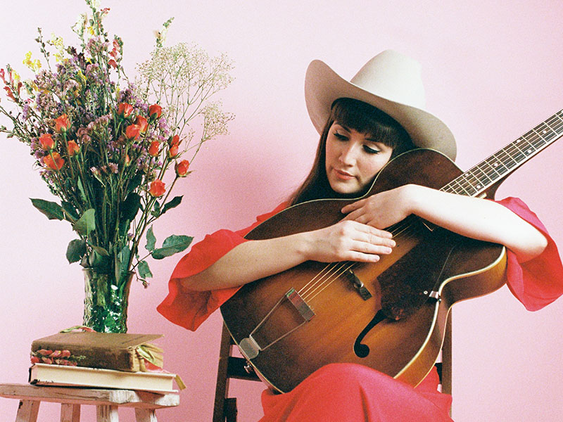 Amy Nelson holds a guitar next to a vase of flowers