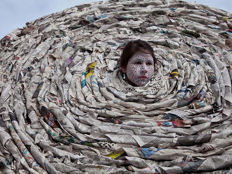 Meryl McMaster's head pokes out of a cirlce of newspaper