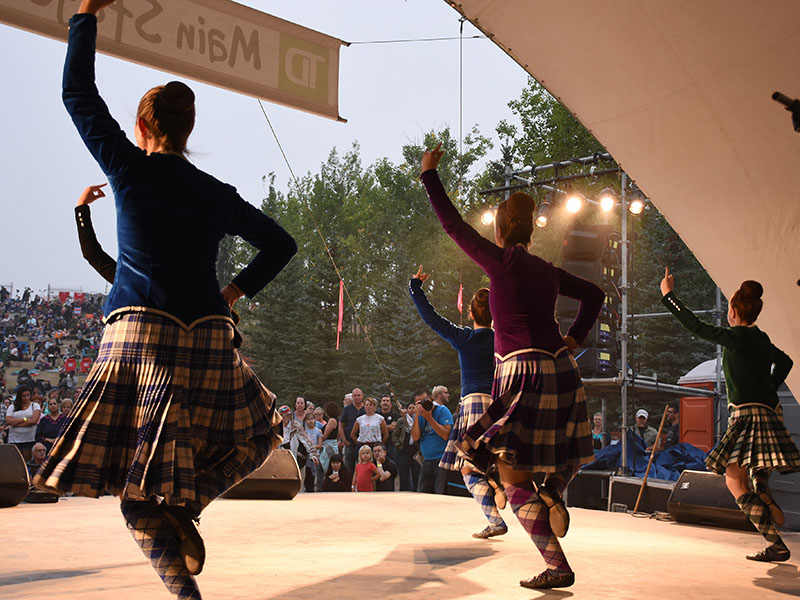 A photo from behind four Highland dancers and the audience watching them perform 