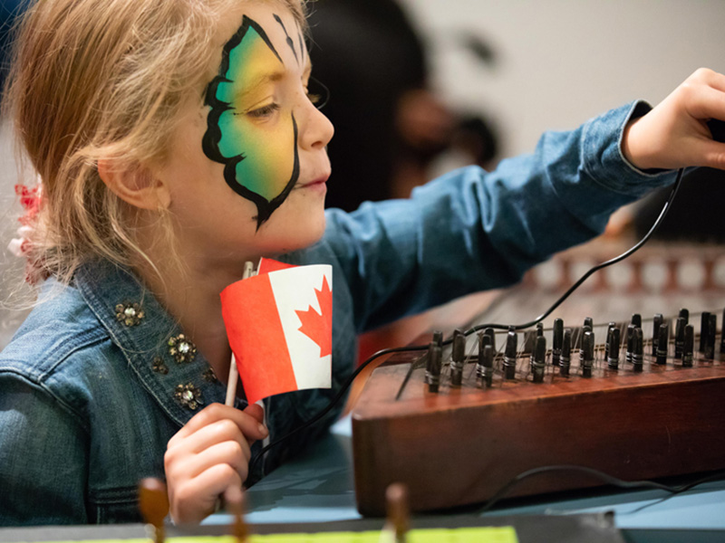 A child with a painted face holds a Canadian flag while exploring Studio Bell