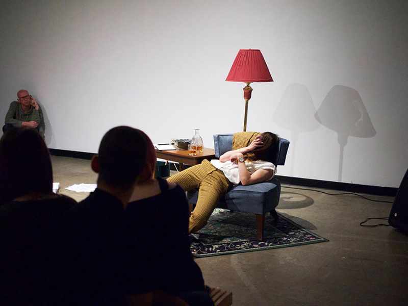 A person slouches in a chair in a performance piece