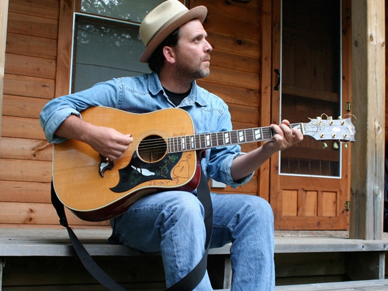 A man plays an acoustic guitar on a front porch.