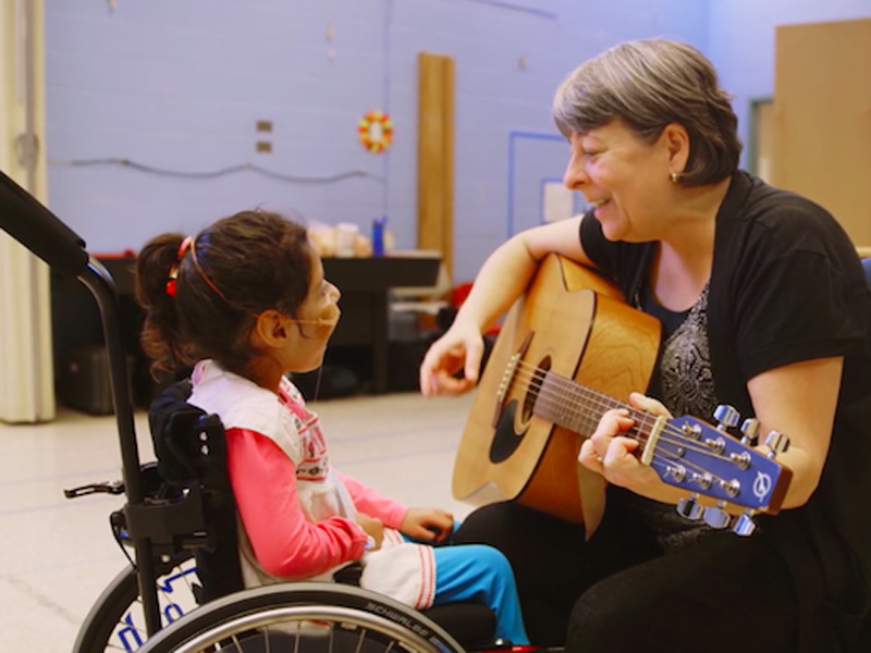 A woman plays guitar to a girl in a wheelchair