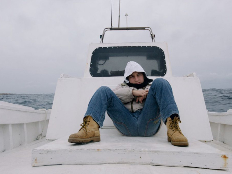 A man sits huddled on an open ship deck