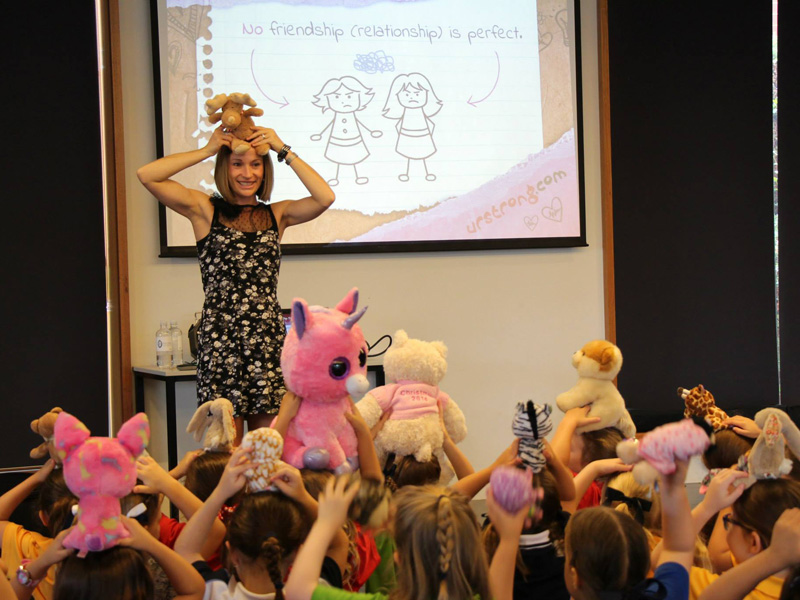 A woman holds up a stuffed animal in a room full of girls