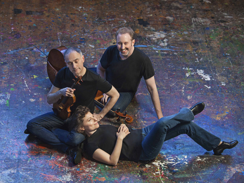 Photo of the Weiss-Kaplan-Stumpf Trio on a paint splattered stage