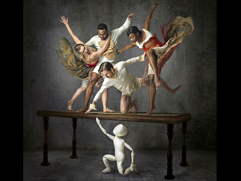 Dancers pose on a table above a blank white puppet