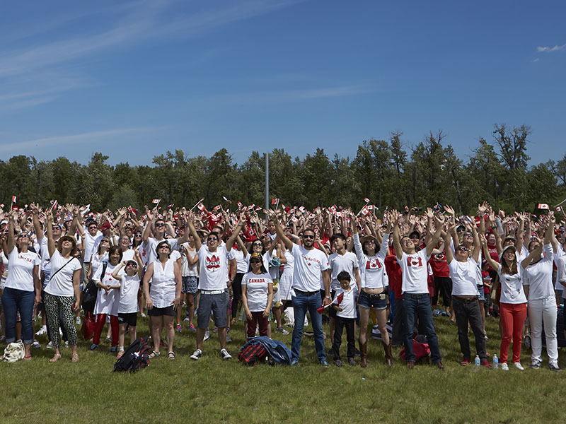 A group photo of hundreds wearing Canada t-shirts and waving flags