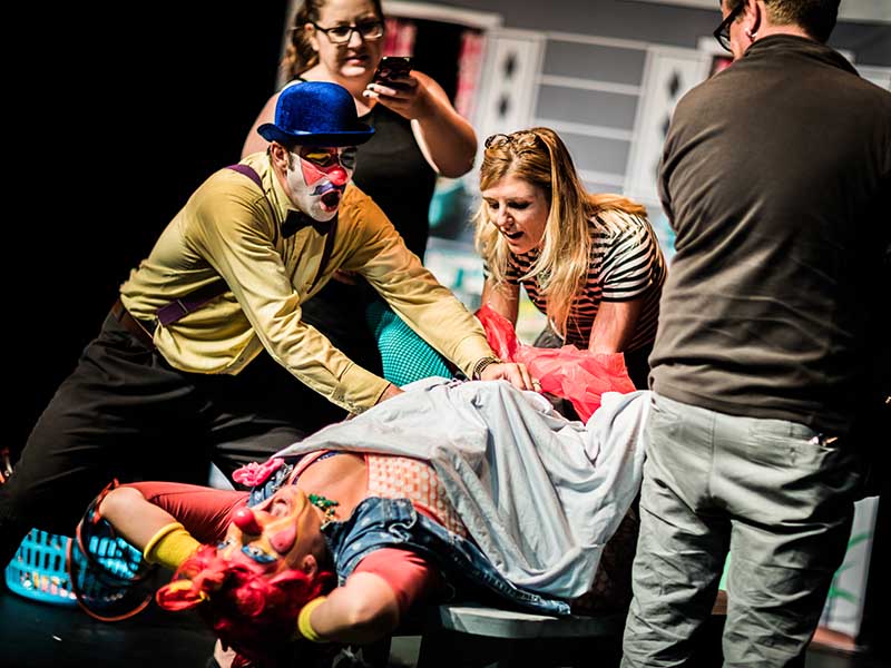 Three people help two clowns, one of whom appears to be giving birth