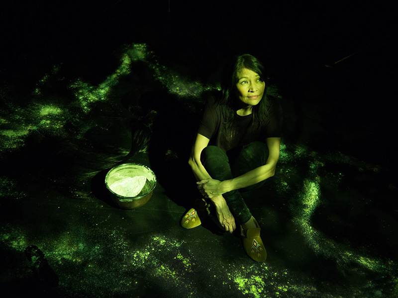 Michelle Thrush sits on stage next to a bowl of white flour