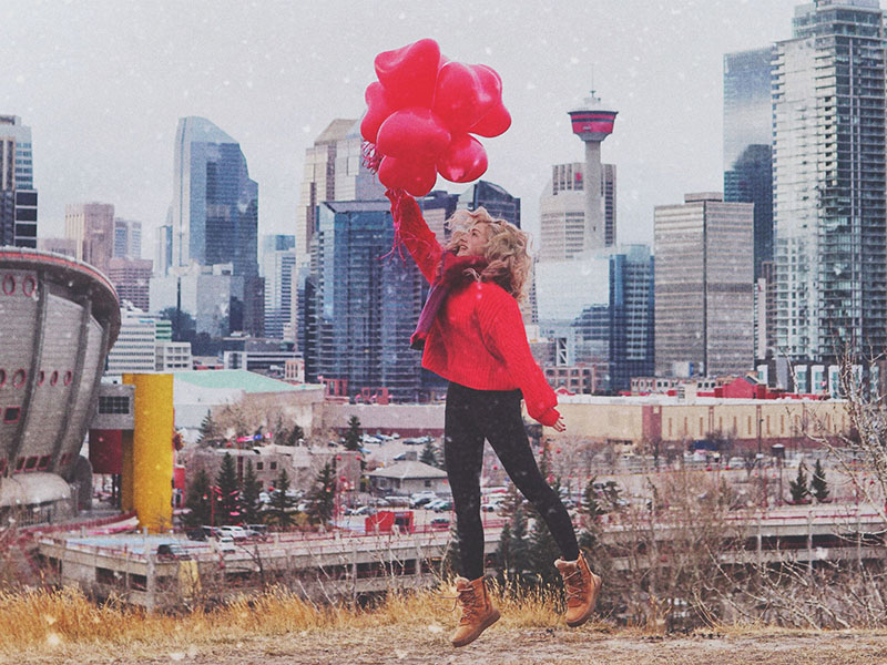 A photo of a woman holding red heart balloons in front of the Calgary skyline