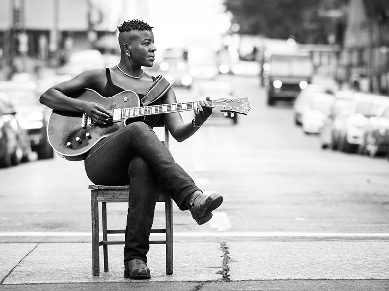 A promo photo of Cécile Doo-Kingué holding a guitar in the middle of a street