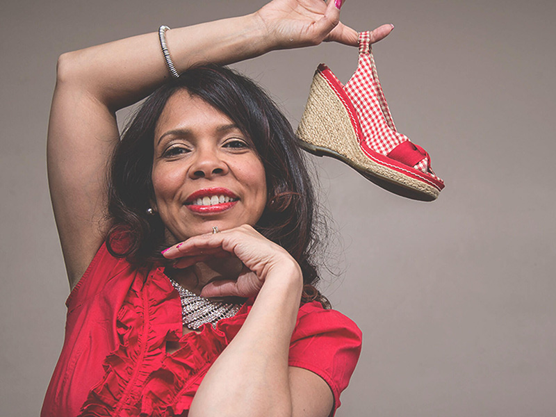 A woman smiles and holds a shoe