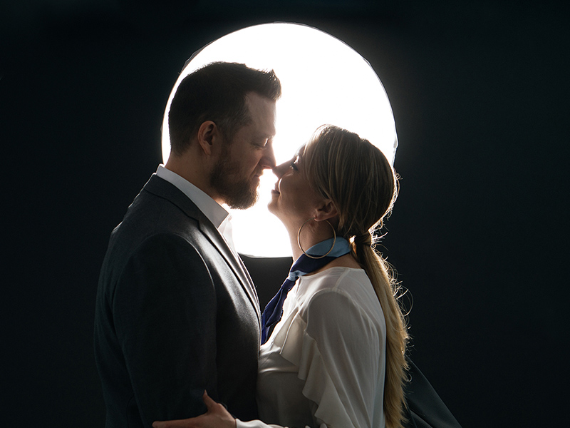 A couple leans in to kiss in front of a bright, round light