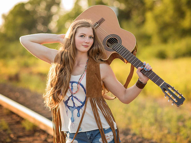 A promo photo of Rebecca Lappa holding a guitar on a railway track