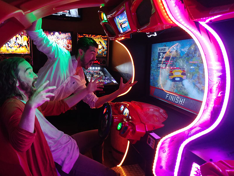 Mark Kunji Ikeda and Richard Lee play a racing game in an arcade