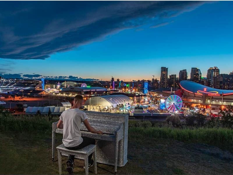 A photo of Hayden McHugh playing the piano during Stampede in front of the Calgary skyline