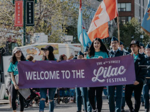 People hold a banner that says, Welcome to the 4th Street Lilac Festival