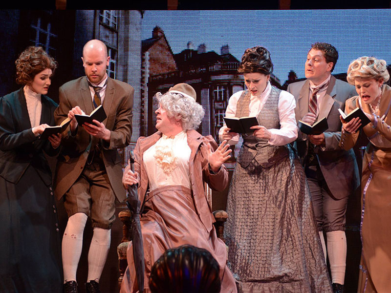 Five people take notes around an exasperated man in drag