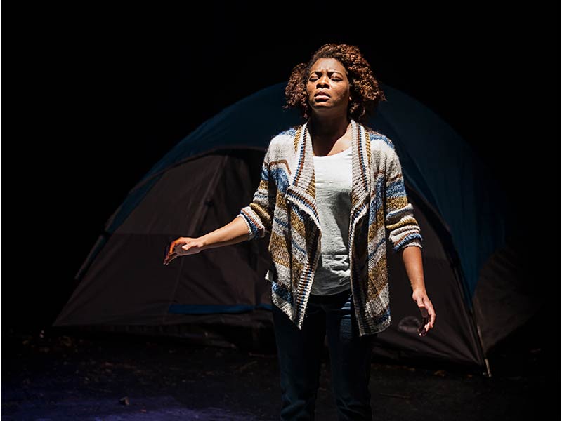 Woman stands in front of tent on production by Sage Theatre