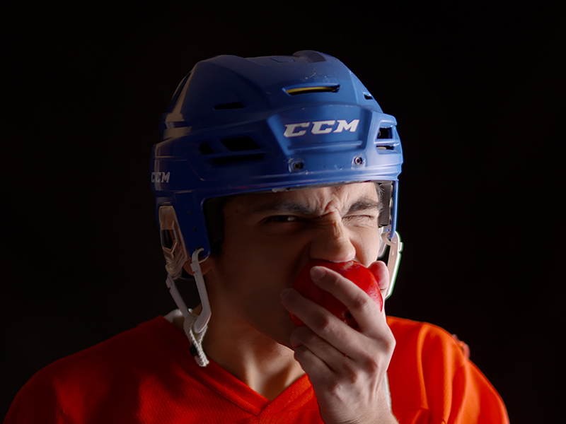 A man in hockey gear eating an apple