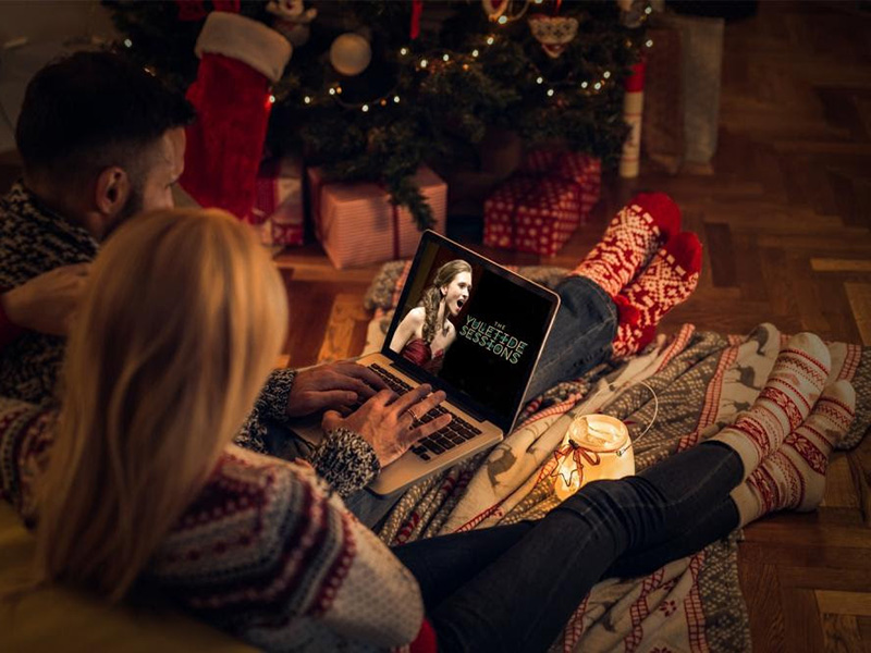 A photo of people decked in Christmas pajamas watching The Yuletide Sessions on a laptop