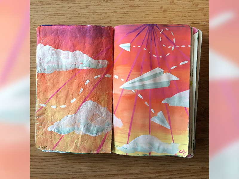 A sketchbook painted with colourful clouds and a paper airplane