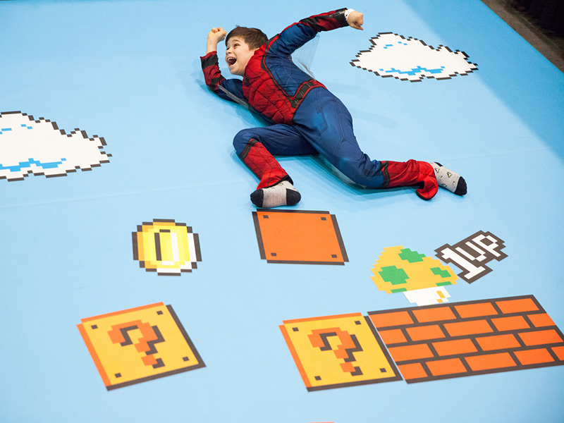 A child in a Spiderman costume playing on a Super Mario themed mat