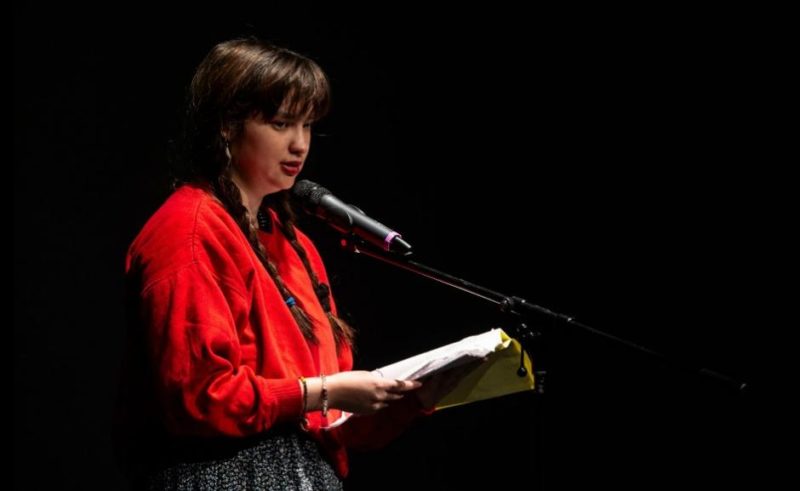 A person on stage reading from a script