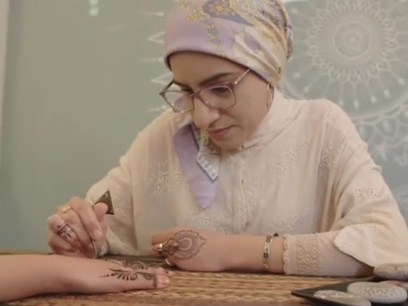 Seema Khan talks with Adora Nwofor while applying henna art on someone's hand