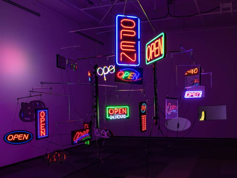 An image of multiple neon open signs in a dimly lit space