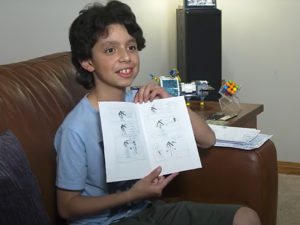 An image of a young boy holding a hand-made comic book