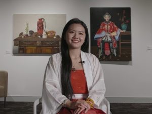 An image of a young woman in front of two works of Asian-inspired art