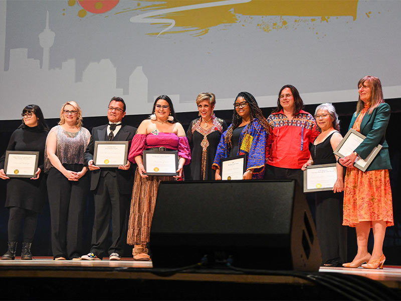 An image of nine people on a stage holding awards