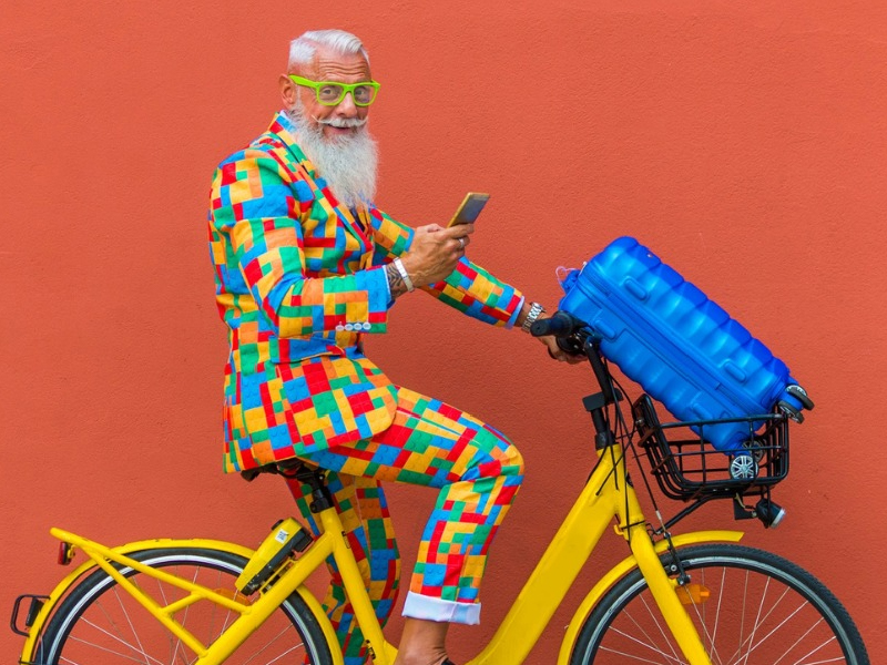 Image of white haired man wearing a patterned suit while on a bicycle and holding cellphone