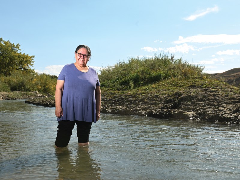 Image of Faye Heavyshield standing in Oldman River in southern Alberta on a clear sunny day