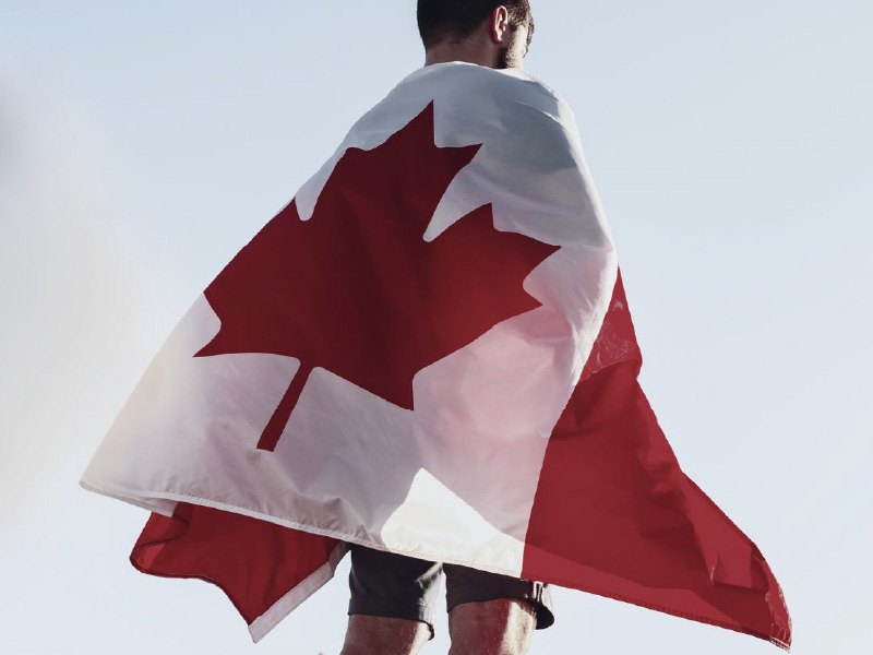 Image of person facing into distance with Canadian flag wrapped around their back
