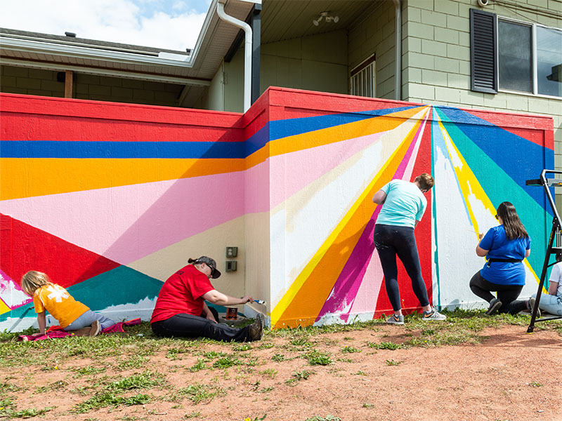 Community members help paint coloured lines to create an abstract landscape.