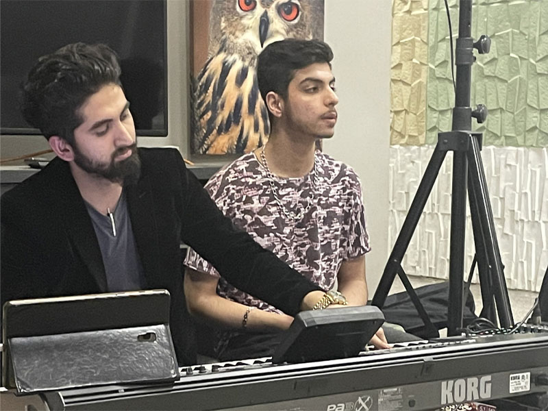 A man plays music on a keyboard while another sings.
