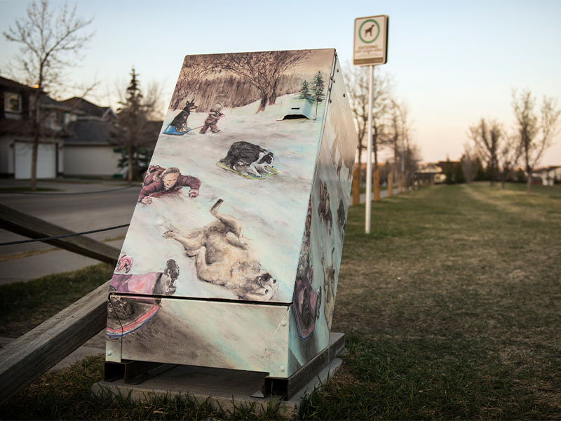 A garbage bin wrapped with artwork of people and dogs sledding down a snowy hill.