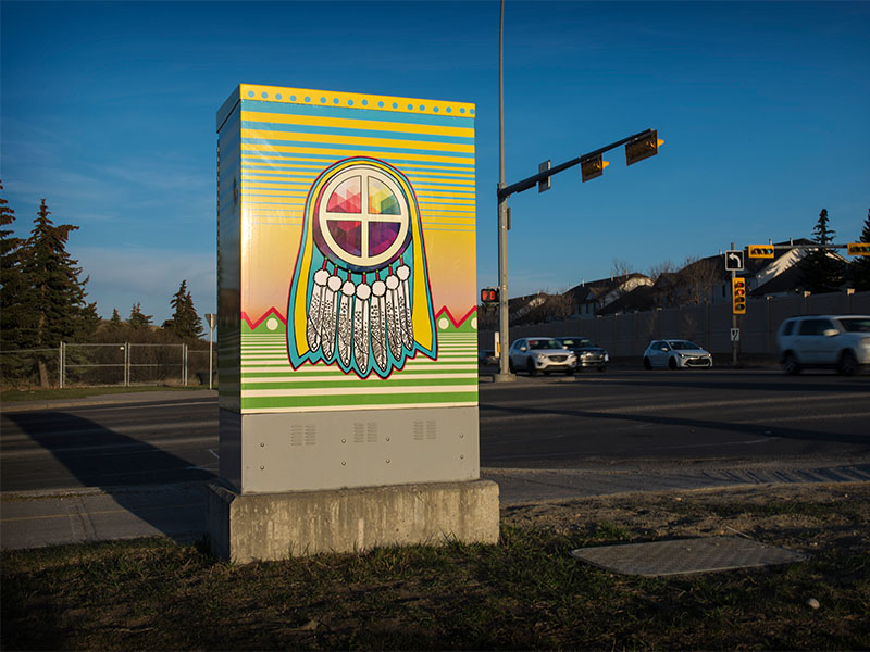 An energy utility box wrapped with First Nations imagery sits at the corner of an intersection
