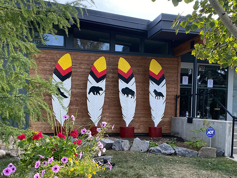 Four sculptures outside the Banff Community Association. Each sculpture is of a feather, and each features a unique animal: an eagle, a bear, a bison and a wolf.