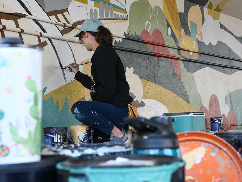 Artist Yiting Hui paints a mural, which features a confluence of people and foods from different cultures.