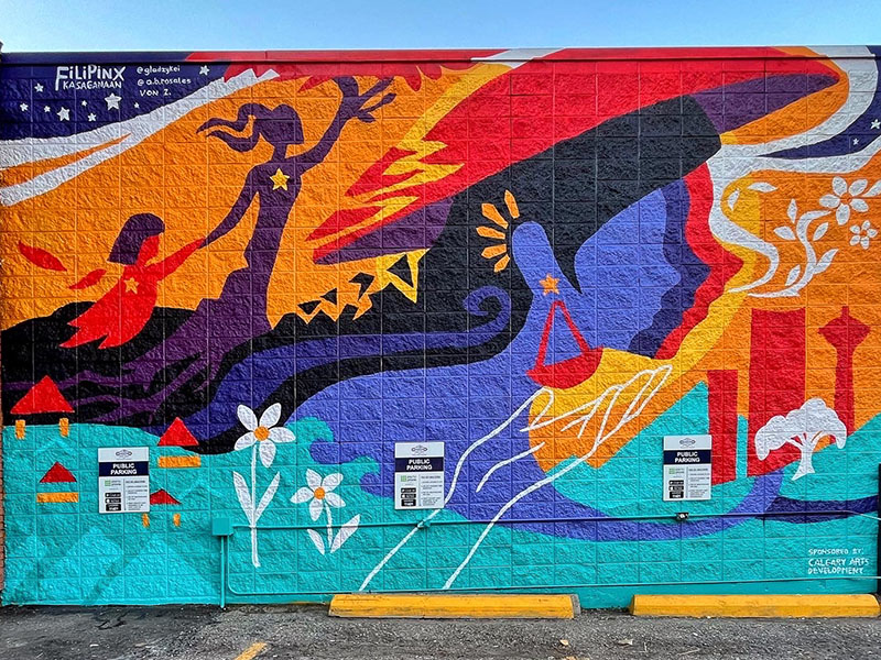 A colourful mural featuring women, hand-in-hand, reaching upward with the Calgary downtown painted behind them.