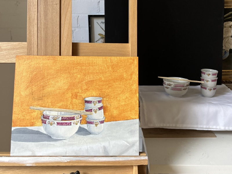 Image of a painting of porcelain bowls with reference material in the background