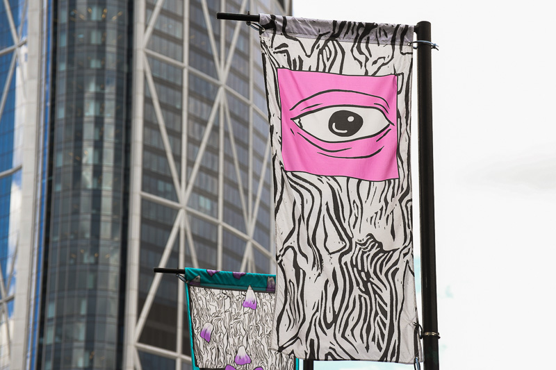 A banner floating on a pole. The banner has a black and white textured background. Near the top is a frame eye with pink skin.