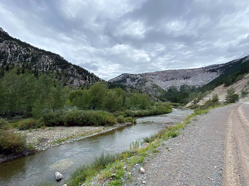 An image of a gravel road aside a river and mountains