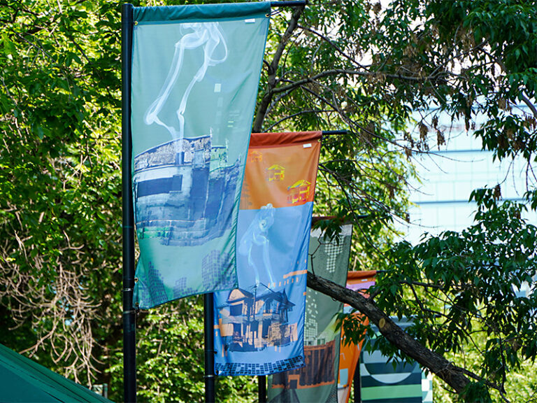Colourful banners in front of bright green foliage along a public street or bridge