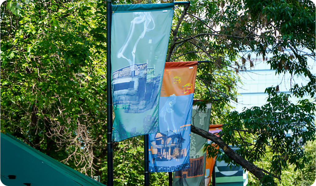 Colourful banners in front of bright green foliage along a public street or bridge